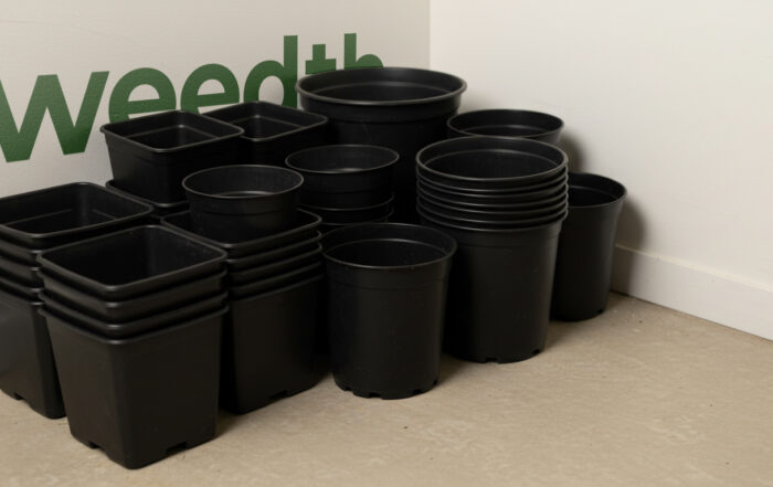 Stacks of empty black plastic pots of various sizes placed against a wall with the Weedth logo in the background.